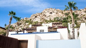 Un edificio con fachada blanca, techo azul y una ladera rocosa al fondo.