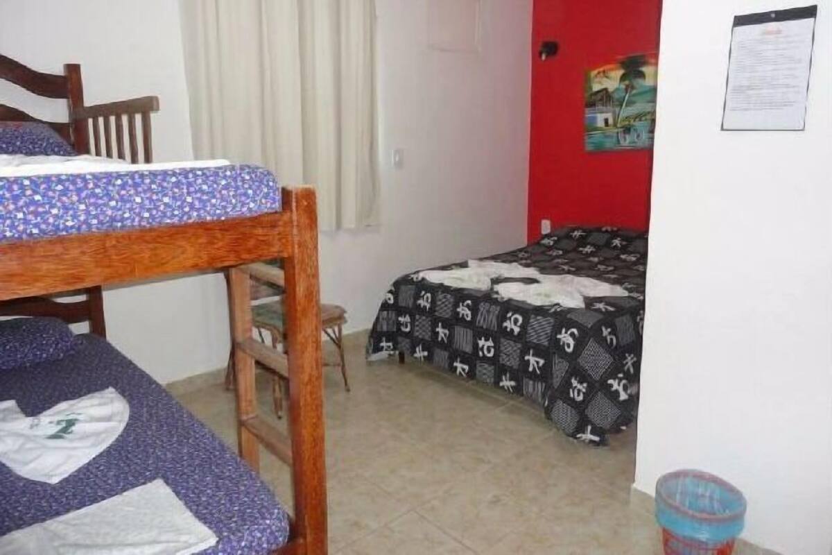 Ein Schlafsaalzimmer mit zwei Etagenbetten, einem Holzbett, einem kleinen Tisch, einer roten Wand mit einem Poster und einem gefliesten Boden.