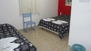 A small, simple room with two beds, a chair, and a red wall. - Pousada Residence Oásis (Maragogi)