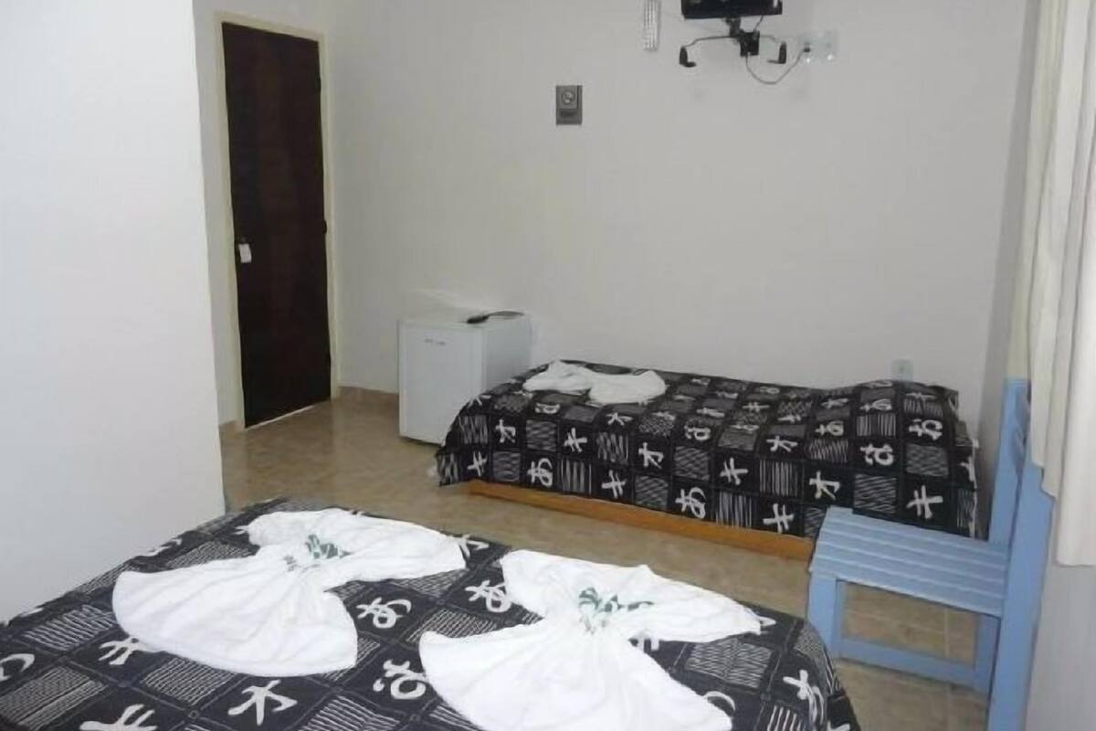 Ein kleines, schlichtes Zimmer mit zwei Betten, einem Schreibtisch und einem Fernseher.