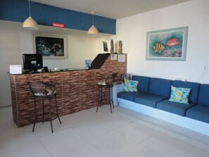 A reception area with a desk, two chairs, a blue sofa, and a painting of fish. - Pousada Residence Oásis (Maragogi)