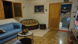 A living room with a blue sofa, a floral sofa, a small table with a vase, and a tiled floor. - Pousada Residence Oásis (Maragogi)