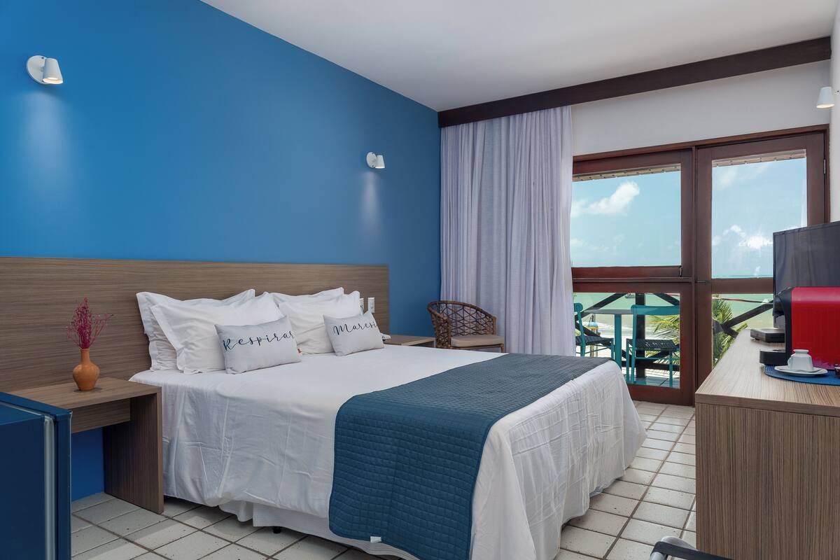 Habitación de hotel con una cama grande, un escritorio, una silla y un balcón con vistas.