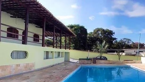 Une piscine avec une terrasse carrelée, un bâtiment doté d’un toit en tuiles et un ciel dégagé.