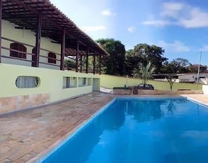 Una piscina con solárium empedrado, un edificio con tejado de tejas y cielo despejado.