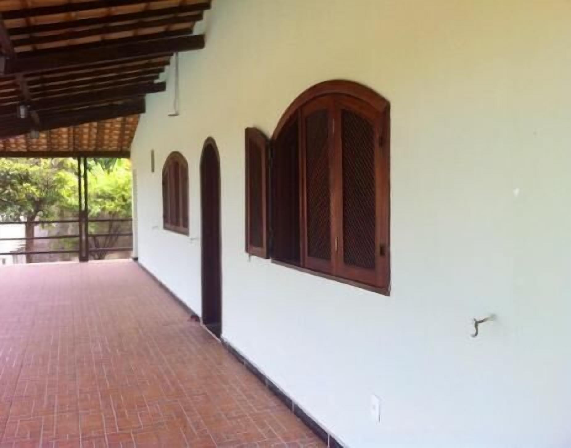 A covered outdoor area with a brick floor, white walls, and wooden-framed windows.
