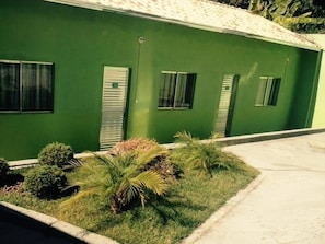 A green building with four windows, a door, and a small garden area with various plants. - Pousada da Lapa (Vespasiano)