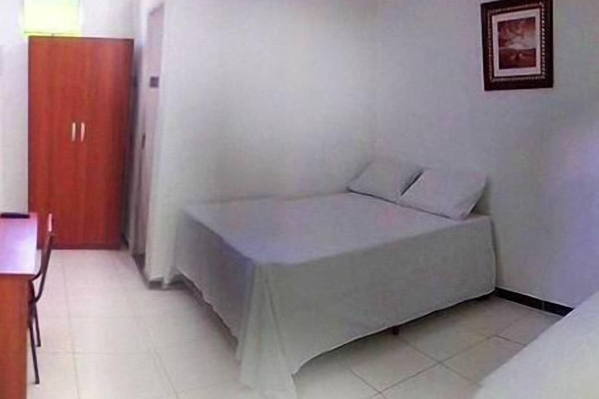 Quarto pequeno com uma cama de solteiro, guarda-roupa de madeira e uma mesa.