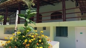 Un bâtiment doté d’un espace extérieur abrité, d’un parterre fleuri avec des fleurs jaunes et d’une porte sur laquelle est apposée une enseigne.