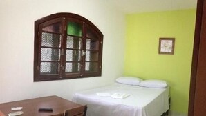 Une petite chambre avec un lit simple, un bureau et une chaise, une fenêtre avec un cadre en bois et un mur vert.