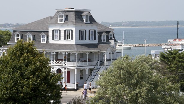 A large, multi-story white building with a grey roof, featuring a balcony and a staircase leading to the upper floors. - Inn at Old Harbor (Block Island)