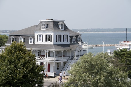A large, multi-story white building with a grey roof, featuring a balcony and a staircase leading to the upper floors.
