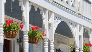 A two-story porch with white railings and hanging flower baskets. - Inn at Old Harbor (Block Island)
