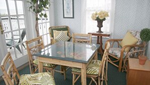 A dining area with a glass table surrounded by wicker chairs with patterned cushions. - Inn at Old Harbor (Block Island)