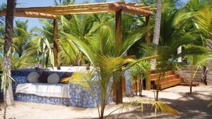 Een strandlounge met een zitgedeelte betegeld met mozaïek, omringd door palmbomen en een houten pergola.