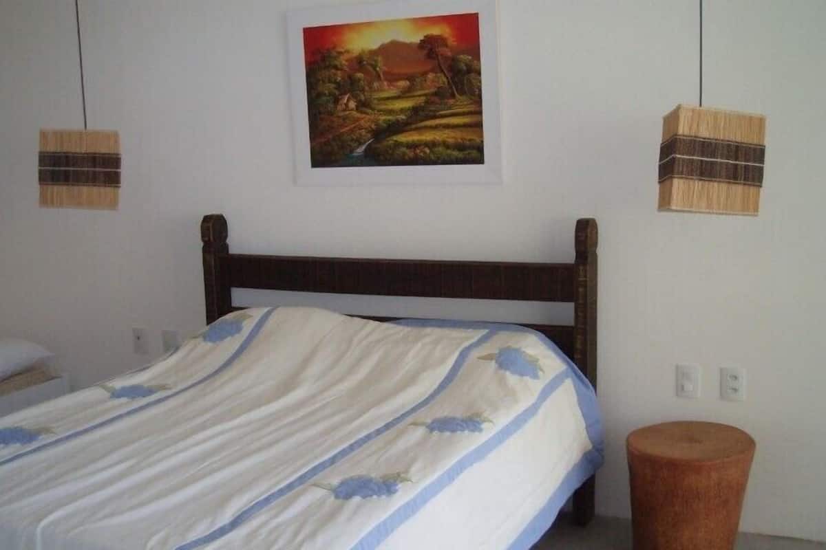 Une chambre à coucher avec un lit en bois, une petite table de chevet, une lampe de chevet, un tabouret en bois et un tableau accroché au mur.