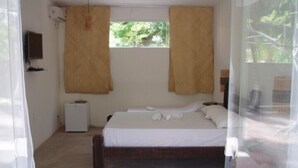 Een slaapkamer met een bed, een klein nachtkastje, een aan de muur bevestigde televisie en een raam met gordijnen.