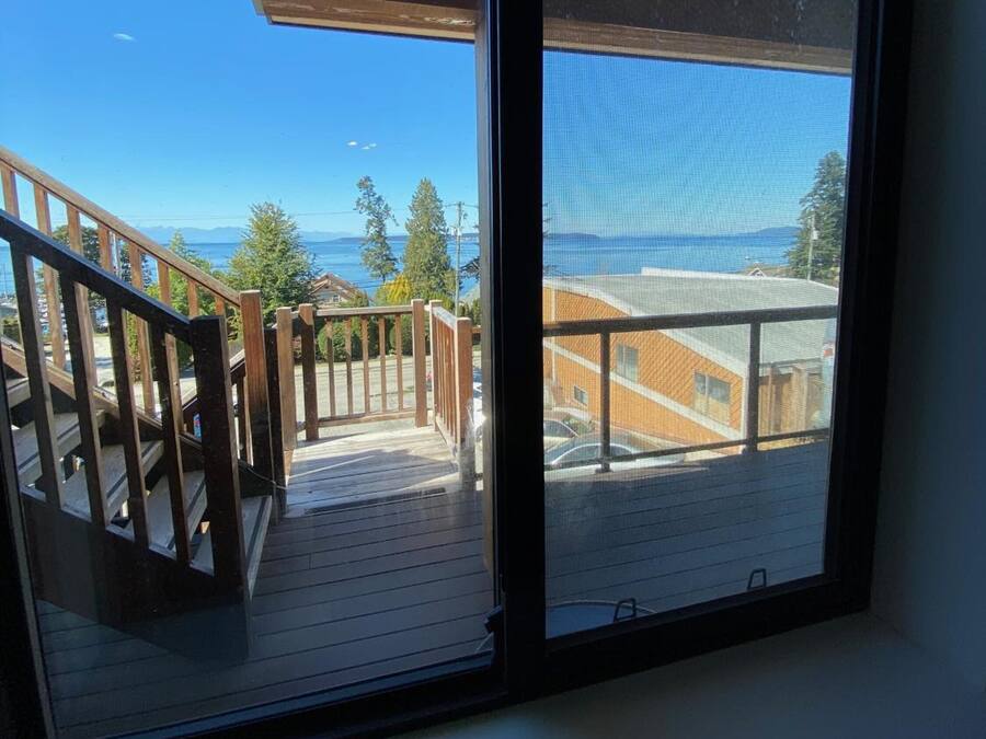 A balcony with a wooden railing, a view of the sea, and a clear sky.