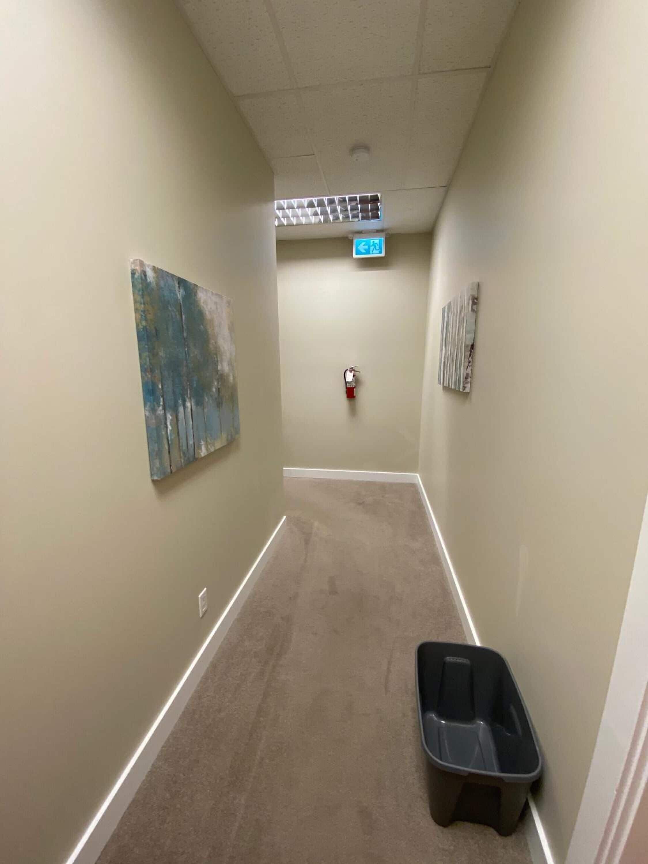 A hallway with beige walls, a fire extinguisher mounted on the wall, a trash bin, and a directional sign.