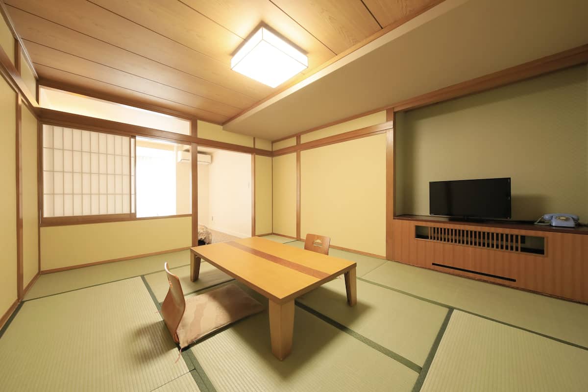 Una habitació japonesa tradicional amb tatami, una taula de fusta baixa, un televisor sobre un suport de fusta i portes corredisses shoji.