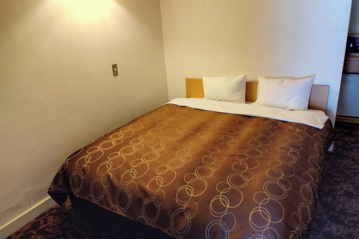 Habitació d'hotel amb un llit gran, un capçal i una tauleta de nit.