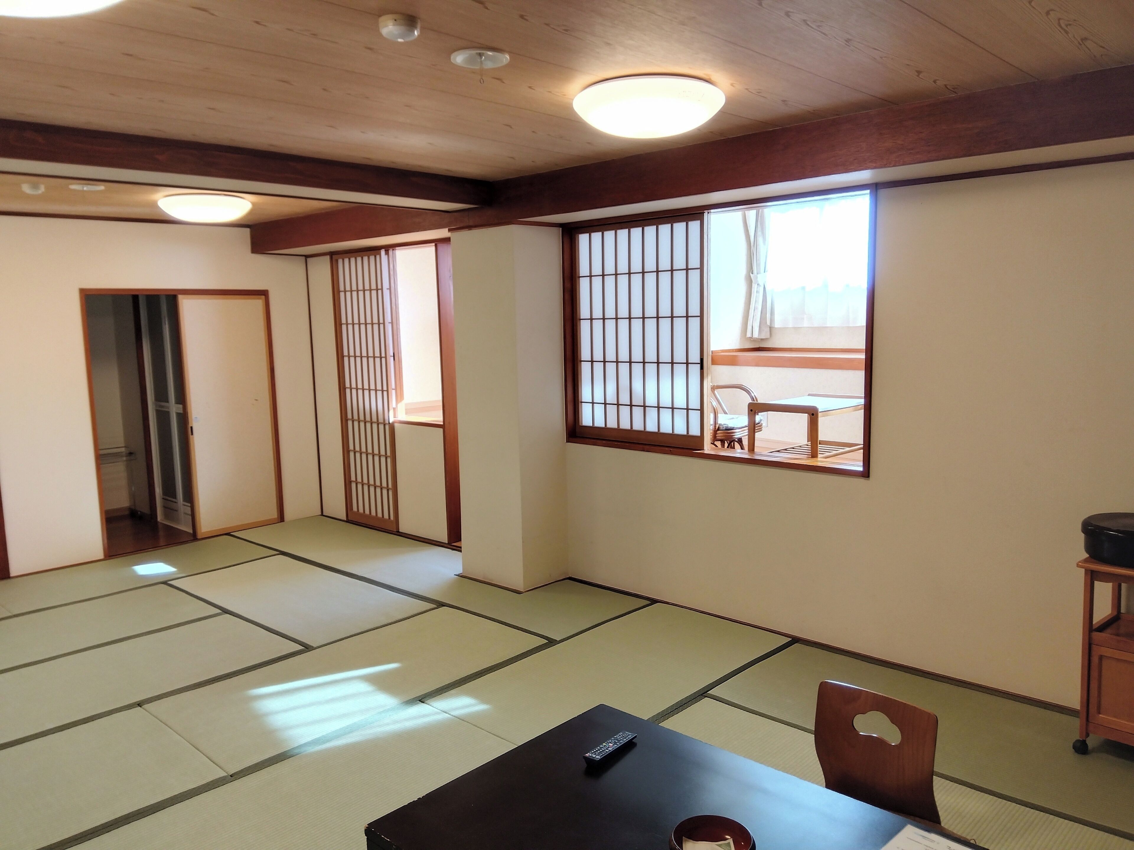 A traditional Japanese room with tatami flooring, a sliding door, a window with shoji screens, and a table with a remote control.