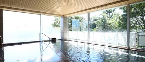 Une piscine intérieure avec des parois en verre transparent, un plafond en bois et un sol carrelé.