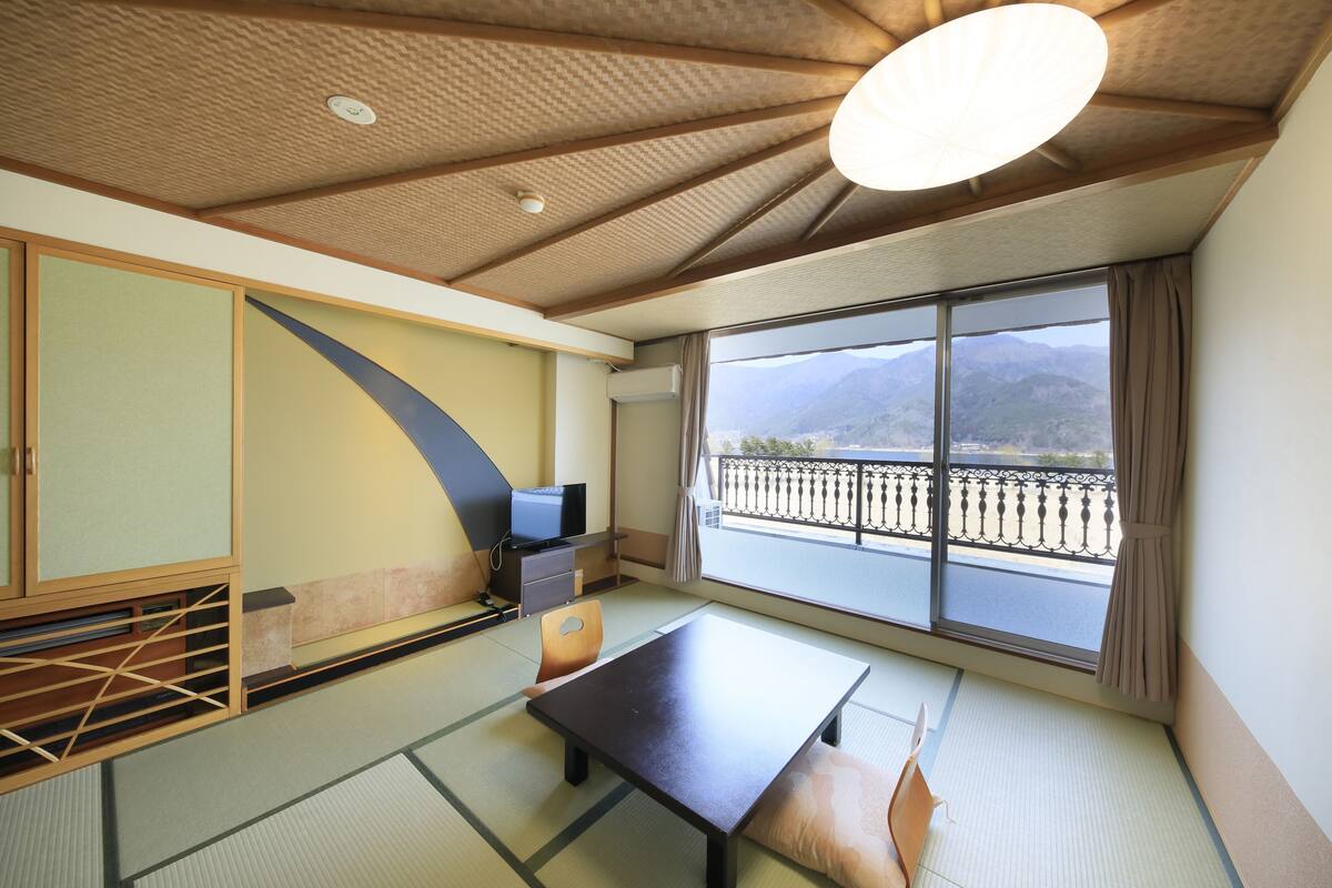 Habitació japonesa tradicional amb sòls de tatami, una taula baixa, una televisió i vista a les muntanyes a través de grans finestres.