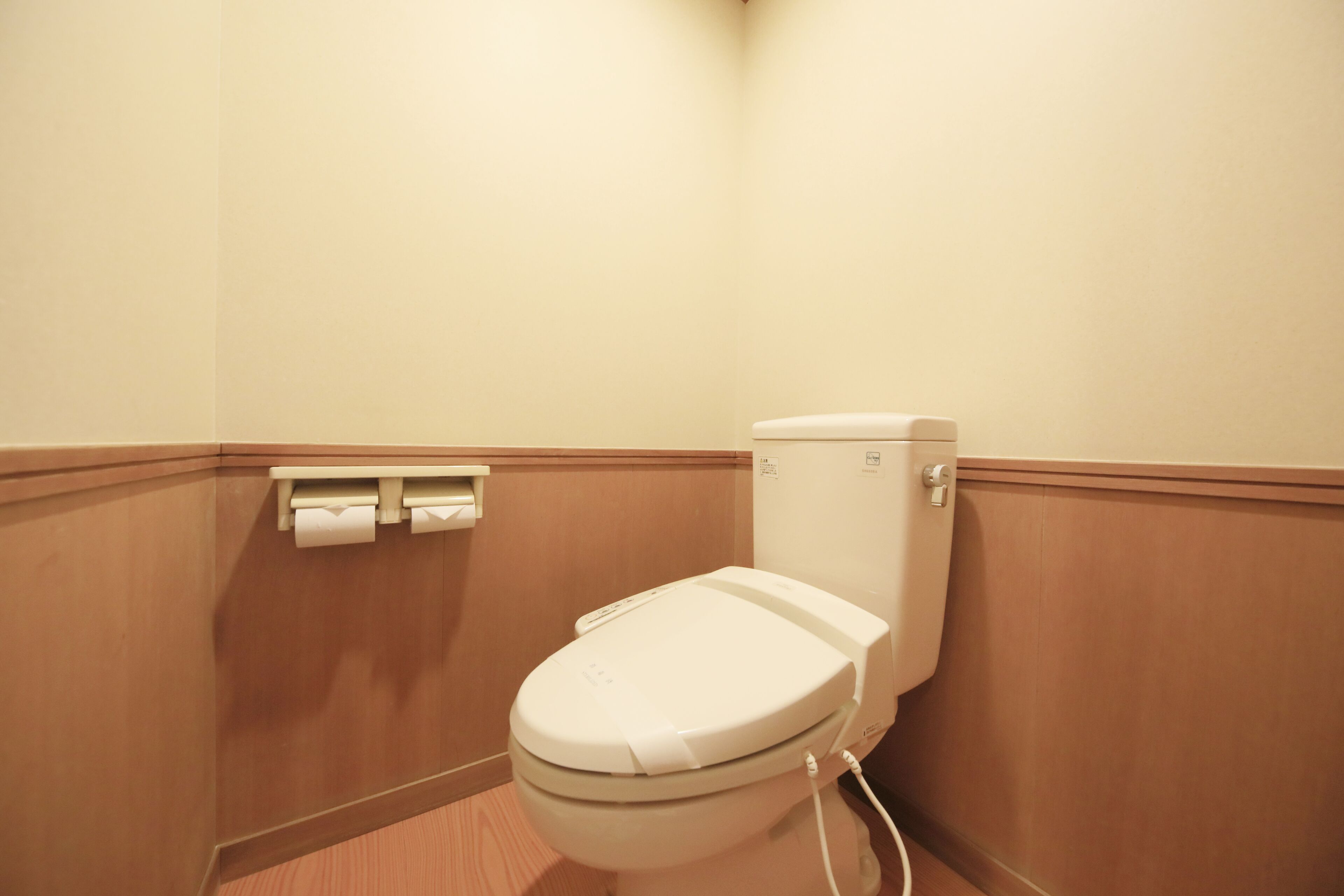 A standard hotel bathroom with a toilet, a paper towel dispenser, and wooden paneling.