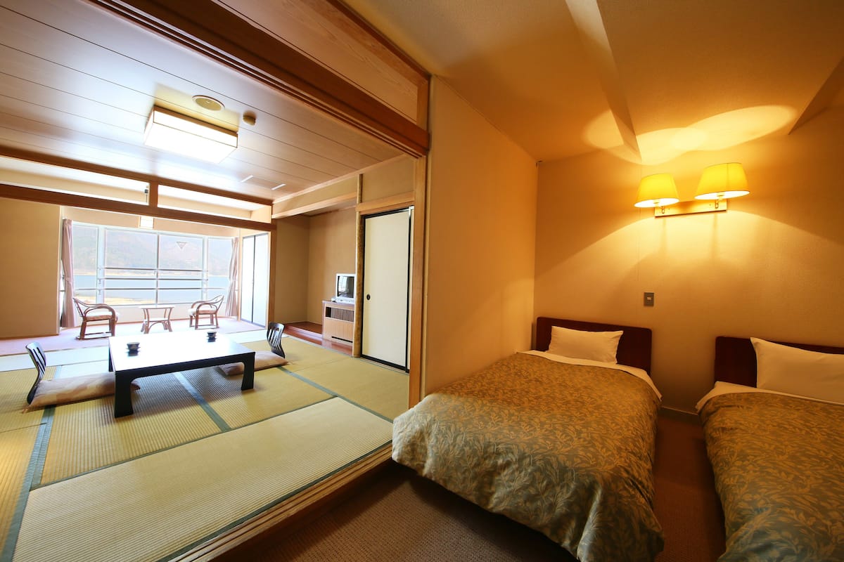 Habitació japonesa tradicional amb fons de tatami, una taula baixa, dos llits i una porta corredissa que dona a un balcó.