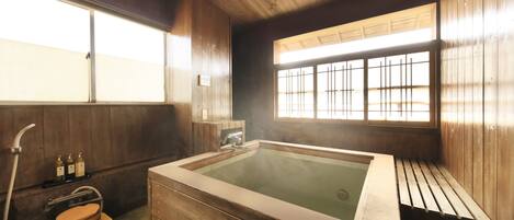 Un balneario de madera tradicional con una bañera de madera grande, un inodoro de madera y una ventana con barrotes.