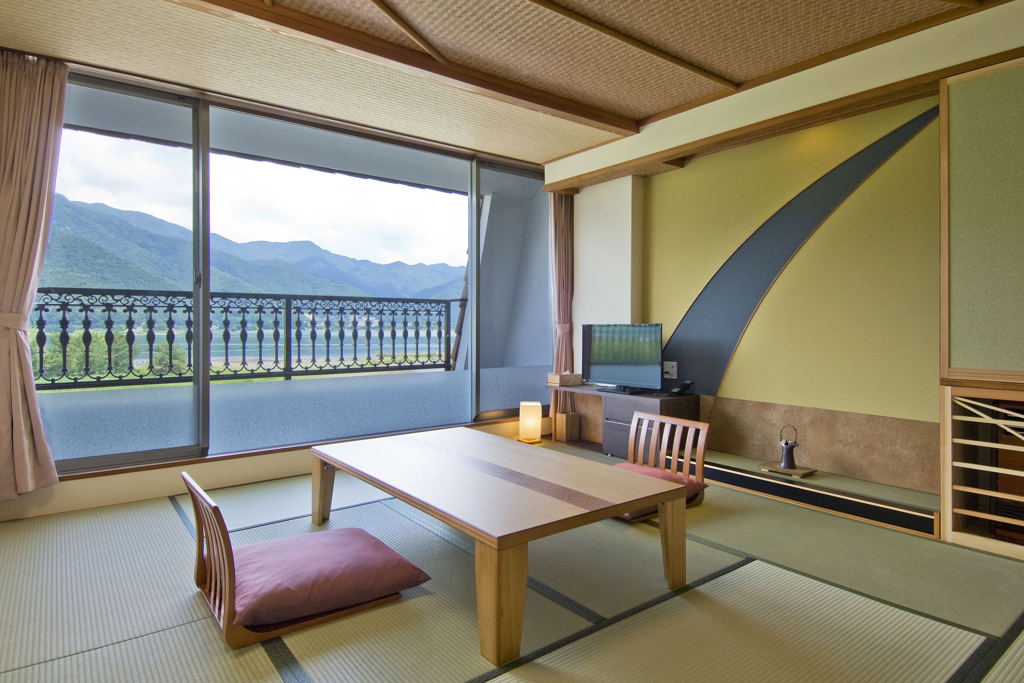 Una stanza tradizionale giapponese con pavimento in tatami, un tavolino basso, una panca imbottita e un televisore.