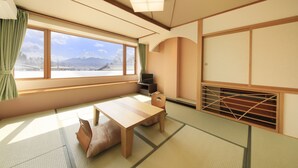 A traditional Japanese room with tatami flooring, a low table, a cushioned bench, a television, and a view of a mountain. - Lakeland Hotel Mizunosato (Fujikawaguchiko)