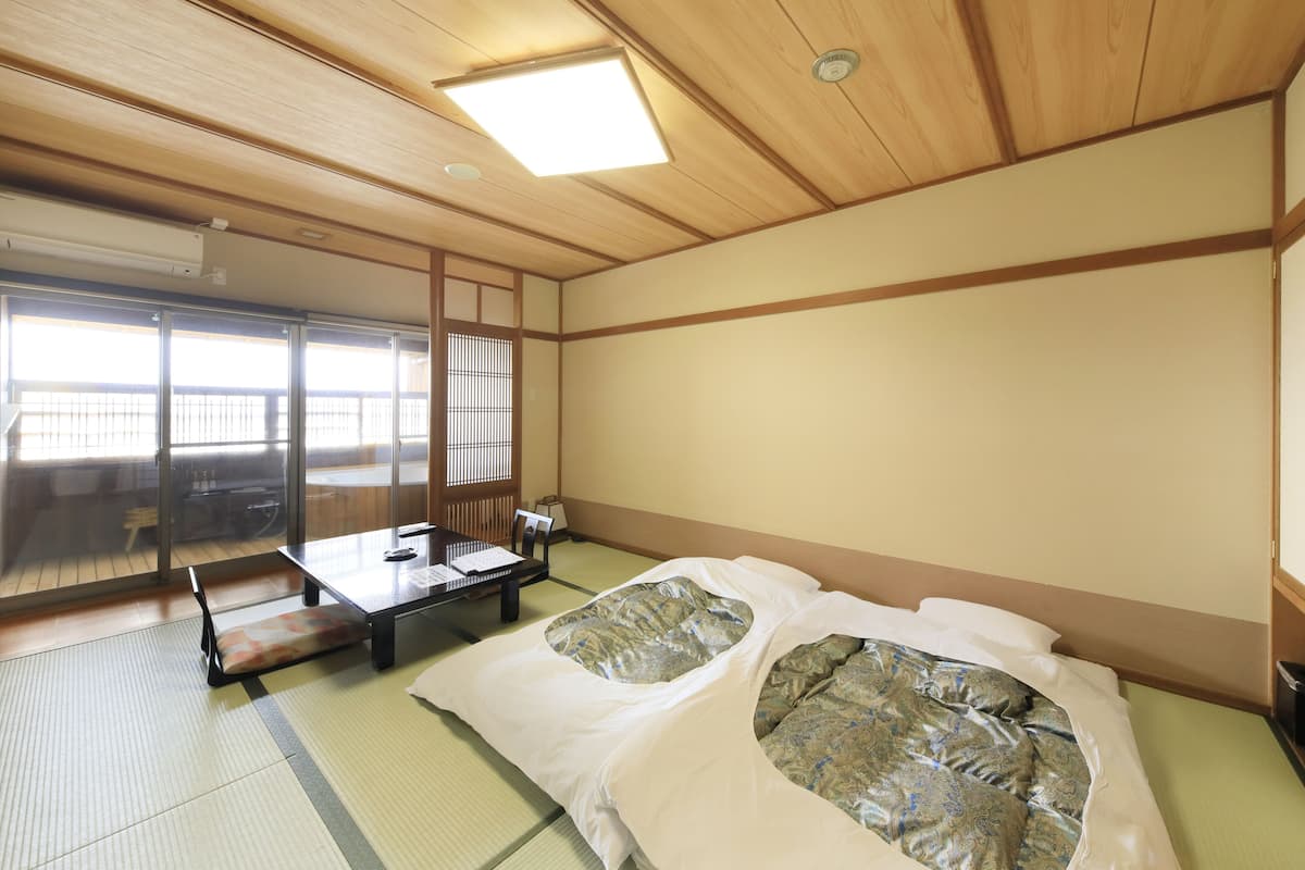 Una habitació japonesa tradicional amb tatami, una taula baixa i un coixí, i un llit amb roba de llit estampada.