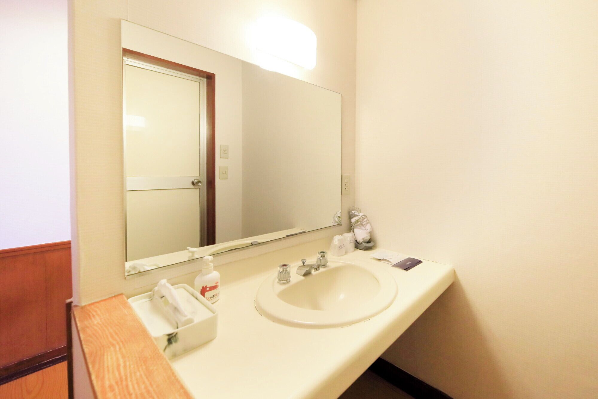 A hotel bathroom with a white sink, a large mirror, and a wooden vanity.