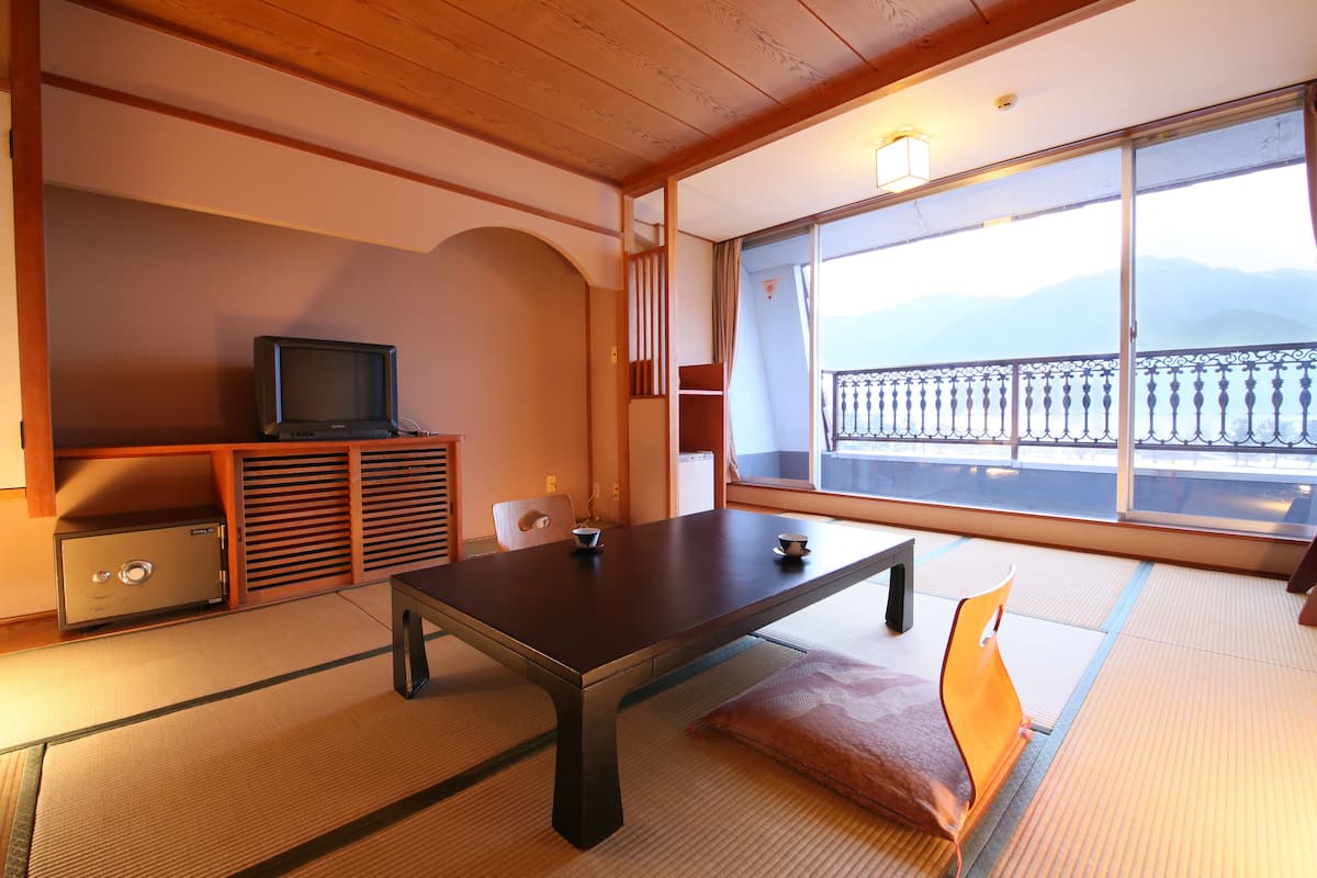Habitació japonesa tradicional amb sòls de tatami, una taula baixa, un televisor sobre un moble i un balcó amb vista a muntanyes.