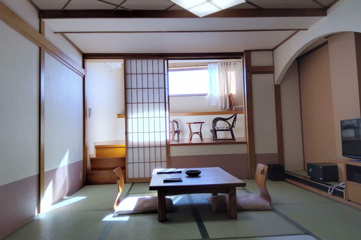 Habitació japonesa tradicional amb sòls de tatami, una taula baixa amb coixins, una porta corredissa i una televisió sobre una estant.