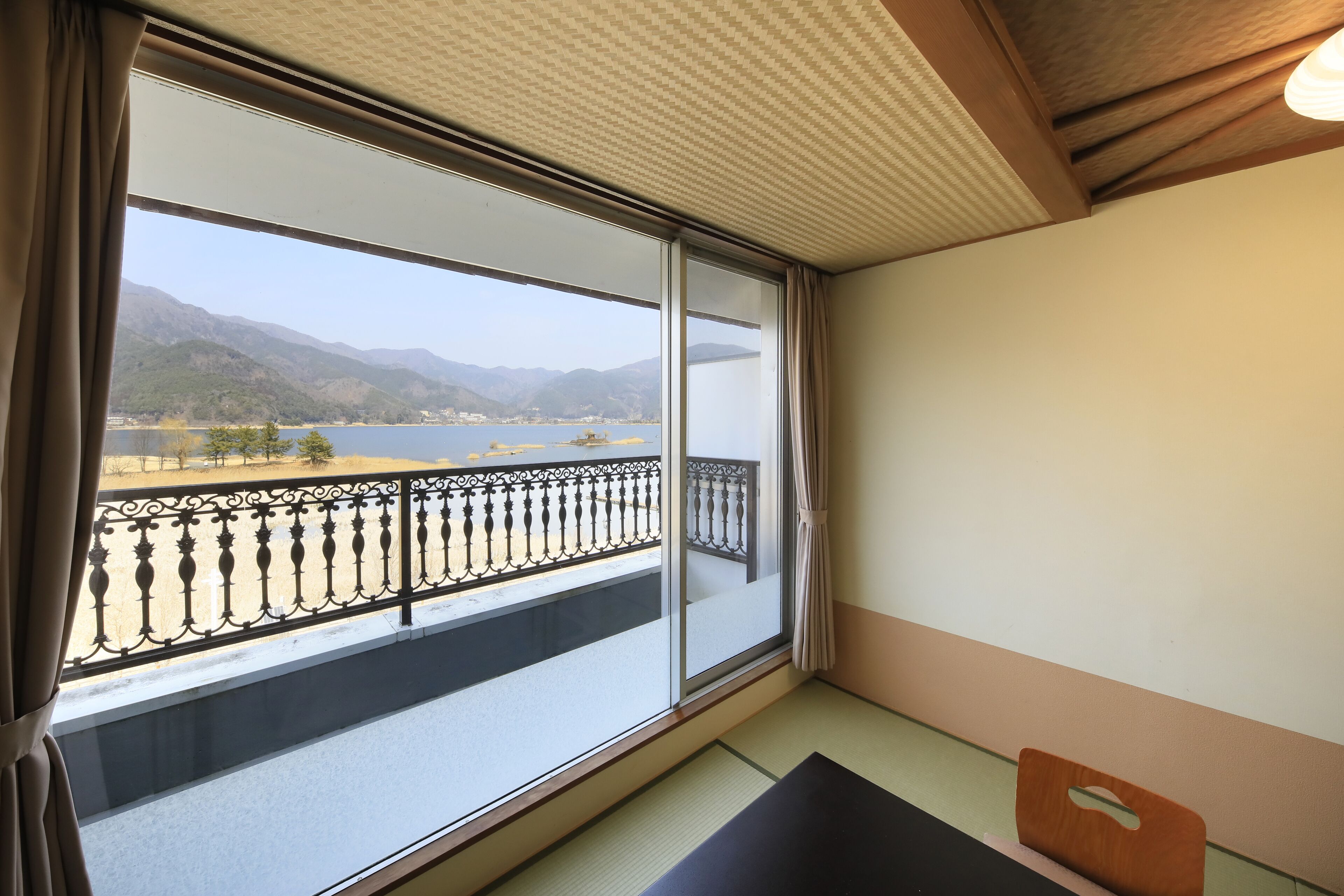 A room with a large window overlooking a balcony with a metal railing, a view of mountains, and a body of water.