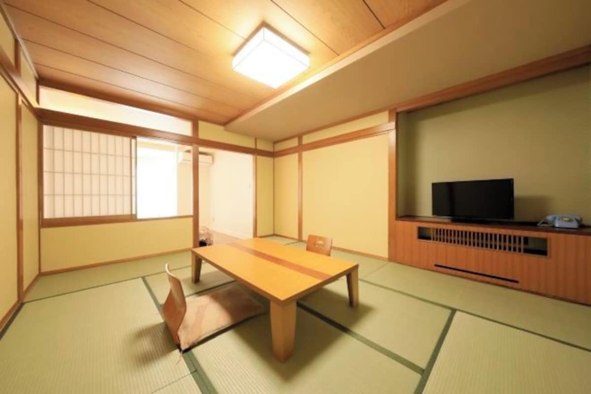 Een traditionele Japanse kamer met tatami vloerbedekking, een lage houten tafel, een televisie op een houten standaard en schuifdeuren van shoji-papier.