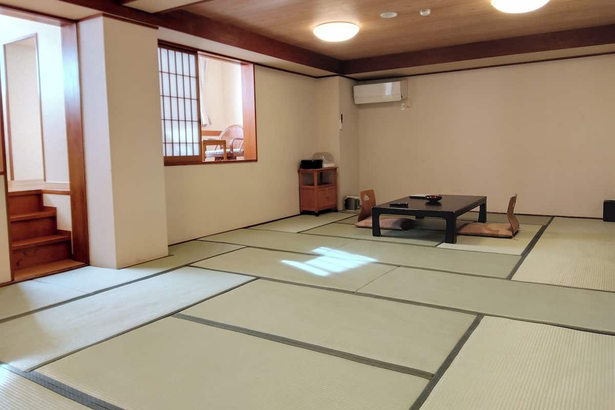 Una habitació japonesa tradicional amb tatami, una taula baixa amb coixins, una porta corredissa i un ventilador de sostre.