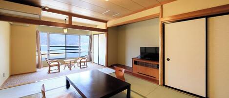 Una habitación con suelo de tatami, una mesa baja, sillas, un televisor y una puerta corredera.