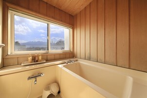 Un baño con bañera, ventana con vistas a la montaña y paredes de madera.