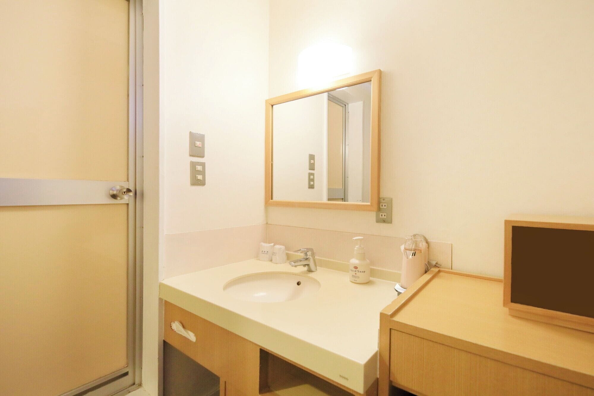 A hotel bathroom with a white sink, a mirror, and a wooden vanity.