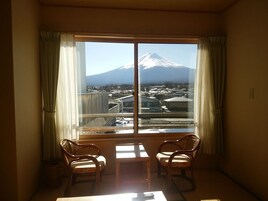 A room with a large window offering a view of a mountain. There are two chairs and a small table in the room.