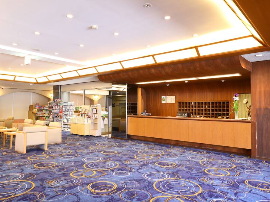 Um saguão de hotel com balcão de recepção, área de estar e carpete com padrões circulares.