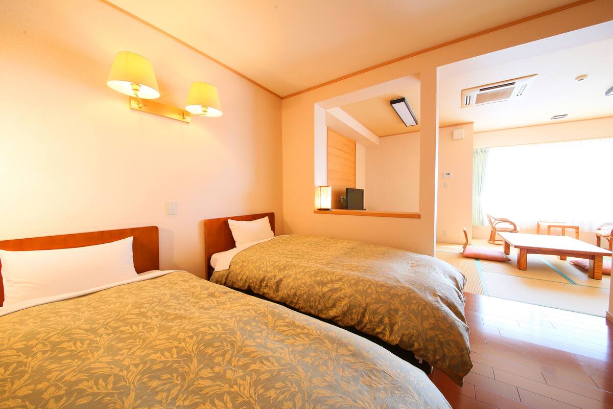 Una habitació d'hotel amb dos llits, una zona de seients amb taula i cadires, i un gran finestral que aporta llum natural.