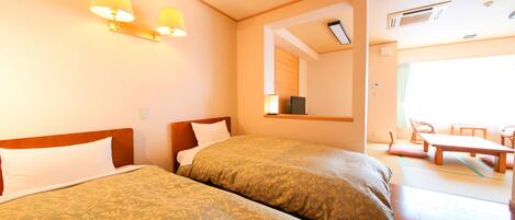 A hotel room with two beds, a sitting area with a table and chairs, and a large window providing natural light.