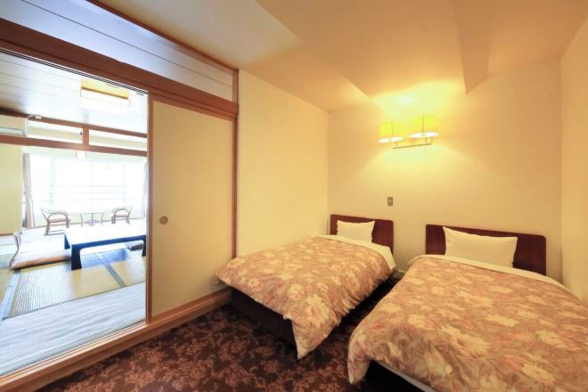 Habitación de hotel con dos camas, puerta corrediza a un balcón y lámpara fijada a la pared.