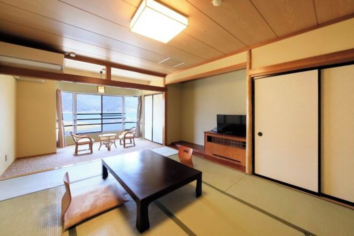 Een traditionele Japanse kamer met tatami vloeren, een lage tafel, een televisie op een houten standaard en schuifdeuren.
