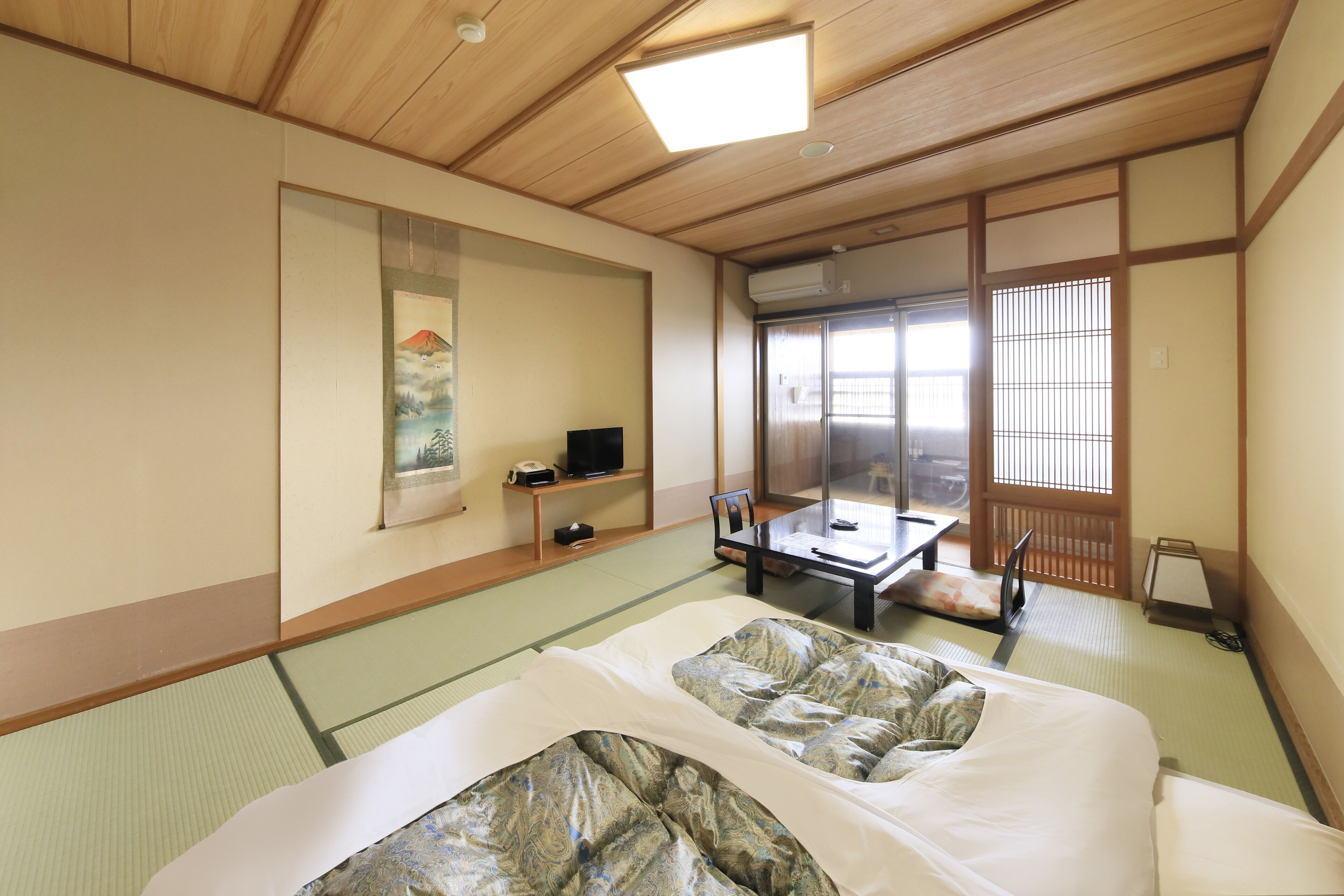 Una habitación japonesa tradicional con suelo de tatami, futón, puertas correderas, televisor y mampara de shoji.